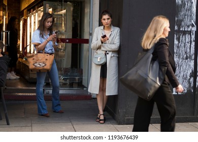 LONDON, United Kingdom- SEPTEMBER 14 2018: People On The Street During The London Fashion Week. Two Girls Stand At The Wall, Look Into Your Phone