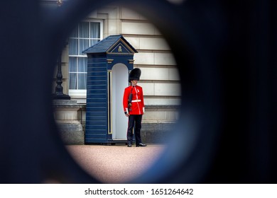 London/England - May 26 2019: A Close Up Portrait Shot Through A Hole Of A Fence Of A Royal Guard Standing At His Garde House And Patrolling Up And Down In Front Of The Palace.