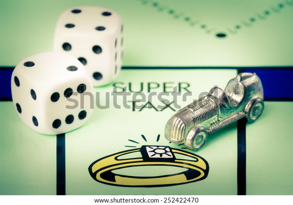 LONDON,UK - FEBRUARY 11,\
2015 : Car token and dice next to the SUPER TAX space in a Monopoly\
game board