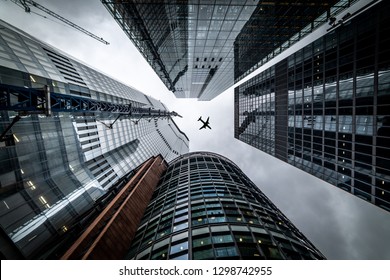 London,UK - January 26th 2019: Silhouette Of A Jet Plane Flying Low Over Three Different Kind Of Architecture With Commercial Office Buildings Exterior In London