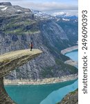 A lone adventurer stands precariously on a natural rock ledge, overlooking breathtaking fjord waters and rugged mountains in Norway. Trolltunga, Norway