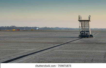 Lone airplane stairs on the apron at airport with airplane in background taxiing - solitude theme of missing the flight