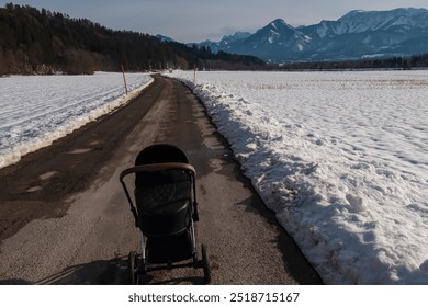 Lone baby stroller on road with panoramic view of majestic snow-capped mountain peaks of Karawanks in Rosental valley, Carinthia, Austria. Winter landscape in remote Austrian Alps. Sunny day walking - Powered by Shutterstock