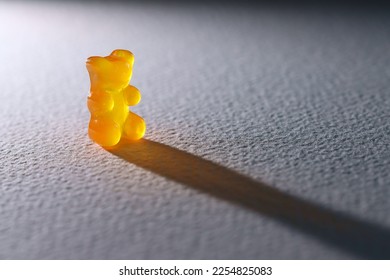 A lone backlit orange gummy bear. casting a long shadow across textured paper. Lost, depressed, sad, children mental health concept. - Shutterstock ID 2254825083