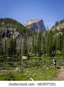 Lone backpacker hiking through Rocky Mountain National Park and stopping by a lily pad-covered pond to take in the view.