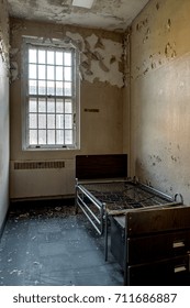 A lone bed sits inside a desolate patient room with a solitary window inside a long abandoned hospital.