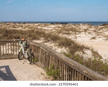 Lone bicycle, with empty coconut shell, on public boardwalk with a view across grassy dunes near vehicles parked along a sandy beach on the Atlantic coast on a sunny afternoon in northeastern Florida