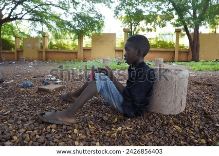 A lone black street boy sitting on the ground with his begging pot staring into space in a run down African city setting