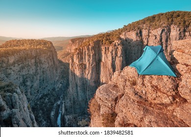 A Lone Blue Tent Is Set On Top Of A Cliff Above A Deep Canyon With Stunning Mountain Views. Concept Of Extreme Rock Climbing And Camping In Dangerous Places