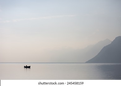 A lone boat on the horizon of the vast of the lake Garda in the northern Italy with light blue morning skies and disappearing mountains in the background.
