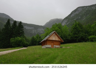 A lone cabin in Slovenia's countrysides surrounded by lush greenery, towering mountains and nearby waterfalls. - Powered by Shutterstock