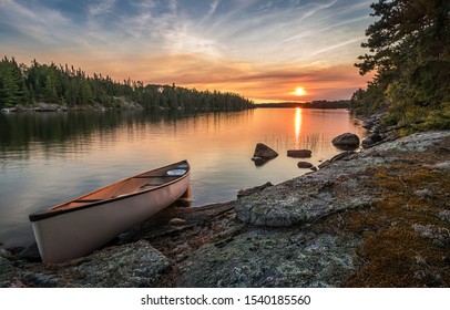 A lone canoe on shore at a peaceful lake at sunset. The odd colored clouds in the background are from a forest fire in Northwest Ontario, Canada in the summer of 2018. - Powered by Shutterstock