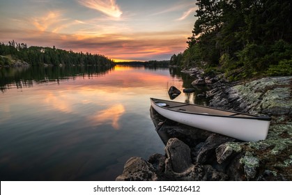 A lone canoe sits on shore on a peaceful lake at sunset. The odd colored clouds in the background are from a forest fire in Northwest Ontario, Canada in the summer of 2018. - Powered by Shutterstock