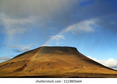 A lone cloud raining down on a volcanic hill on a sunny day creating the rainbow. A pretty and beautiful image of a rugged landscape and hard for life. South of Iceland.