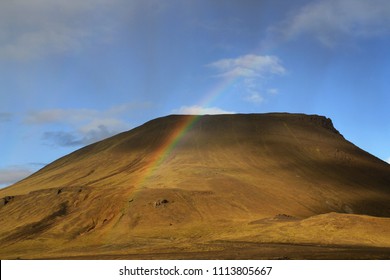 A lone cloud raining down on a volcanic hill on a sunny day creating the rainbow. A pretty and beautiful image of a rugged landscape and hard for life. South of Iceland.