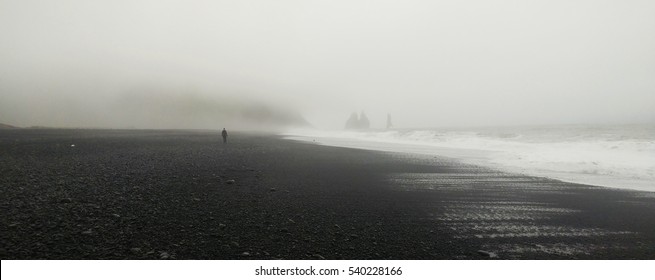 Lone distant figure walking through the fog on the black beach - Vik, Iceland - Powered by Shutterstock