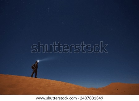 A lone explorer, guided by a lantern, embarks on a celestial journey beneath the desert's night sky, captivated by the cosmic wonders overhead