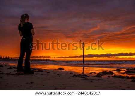 A lone figure stands on a beach at sunset, immersed in the vibrant hues of the sky.