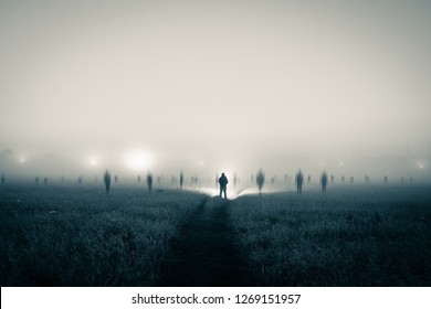 A lone figure with a torch standing in a field as ghostly blurred figures appear on a spooky, misty night. With a duo tone high contrast edit. - Powered by Shutterstock