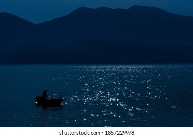 A Lone Fisherman On A Small Boat At Night.