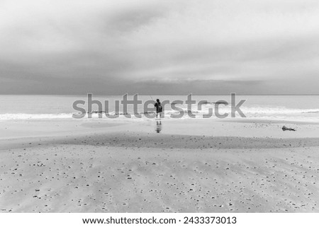 Lone fisherman at the water's edge on a beach with the sky completely overcast