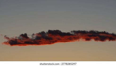 Lone fractus cloud study, a deep fiery crimson, gathers the last remaining rays of sunlight at magic hour as darkness falls. 