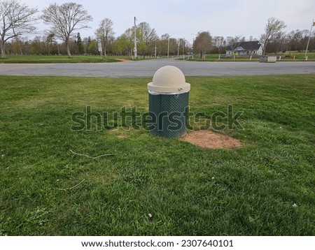 A lone garbage can sitting in a grassy area at a park.