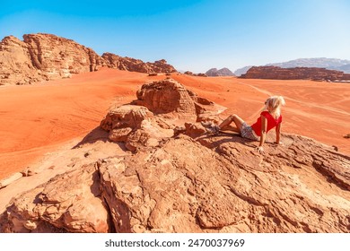 Lone girl traveler sits among the majestic landscapes of Wadi Rum desert in Jordan, reflecting in solitude against the vast, red sands and towering rock formations with Cow Rock landmark - Powered by Shutterstock