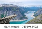 A lone hiker stands on the edge of the Trolltunga cliff in Norway, overlooking a vast, blue fjord. Asian women at Trolltunga, Norway