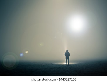 A Lone Hooded Figure Standing In A Field On A Spooky, Foggy Night With UFOs Floating In The Sky.