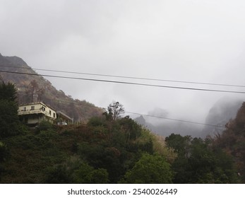 A lone house sits on a hill surrounded by misty mountains and lush greenery, creating a serene and isolated scene, reminiscent of quiet mountain retreats. - Powered by Shutterstock