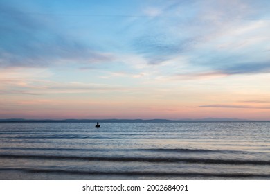 A Lone Iron Man Seen Off The Beach At Crosby At Hight Tide At Dusk In April 2021.  He Is Part Of Another Place, The Art Installation On Crosby Beach Near Liverpool.