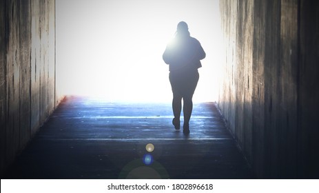 A lone isolated figure fading away heading or walking towards a bright light at the end of tunnel. Grief, death, dying suicide, faith concept. Crossing over