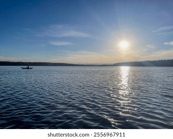 A lone kayaker paddles across a serene lake under a soft sunset, surrounded by distant forested hills and a calm atmosphere. - Powered by Shutterstock