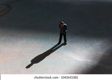 Lone Man In Empty Space With Dramatic Shadow. Looking Down At Feet, He Has A Look Of Guilt Or Shame. Businessman Guilty Of White Collar Crime Or Dishonesty. Silhouette Of Unrecognizable Shadow Man. 