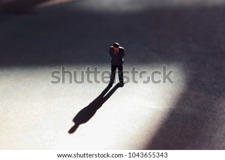 Lone man in empty space with dramatic shadow. Looking down at feet, he has a look of guilt or shame. Businessman guilty of white collar crime or dishonesty. Silhouette of unrecognizable shadow man. 