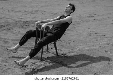 Lone Man Sitting On Chair In Desert. Black And White