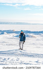 A lone man in a warm jacket and backpack stands in the middle of a snowy desert on a frozen river on a sunny winter day