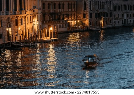 Lone motorboat floats the Grand Canal in Venice in glowing lights against the backdrop of blue water on a summer evening. Concept of romantic tourist trips in the ancient city of Italy. Copyspace