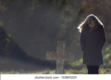 Lone Mourner Graveside. Mourning Widow Dressed In Black With Head Bowed In Cemetery. Middle-aged Grieving Person Dressed In Black Standing By Grave. Since Woman Paying Respects To The Dead. Copy Space