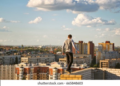 A Lone Roofer Walks Along The Edge Of The Roof Fence On A High-rise Building. Courage And Adrenaline.