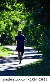 A Lone Runner Runs Along A Paved Path In The Woods.