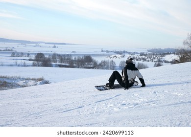 A lone snowboarder sits on a snowy slope and looks ahead. Copy space.                                - Powered by Shutterstock