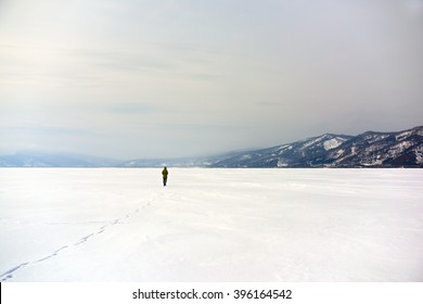 Lone stranger walking his path in the middle of snow white nowhere with distant mountains in background