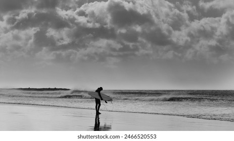 a lone surfer standing by the ocean  with dramatic cloudy sky above him - Powered by Shutterstock