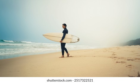 A lone surfer stands on a misty beach, holding his surfboard and looking at the waves. Serene and peaceful scene. - Powered by Shutterstock