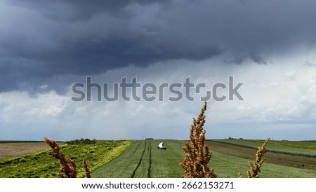 A lone tractor toils beneath brooding storm clouds, embodying autumnal equinox mysteries and agrarian resilience in emerald fields