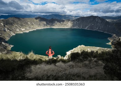 A lone traveler gazes out over the breathtaking Quilotoa Crater Lake in Ecuador. The vibrant turquoise waters of the lake contrast against the rugged, mountainous landscape, creating a serene. - Powered by Shutterstock