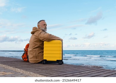 A lone traveler rests on a seaside boardwalk, contemplating the journey ahead with a yellow suitcase at sunset - Powered by Shutterstock