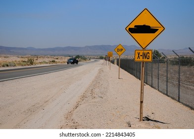 A Lone Truck Rolls Down A Desolate Desert Highway In USA. A Road Sign Warns Of Possible Military Tank Cross Traffic. 